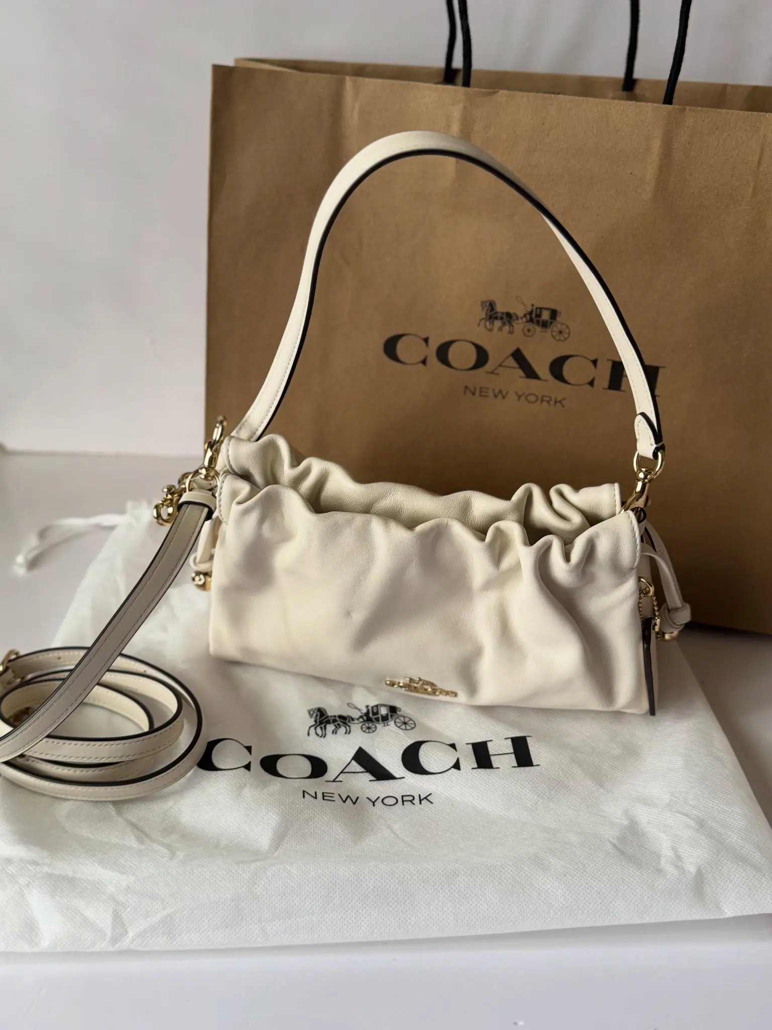 Soft ivory Coach shoulder bag in front of its branded dust bag